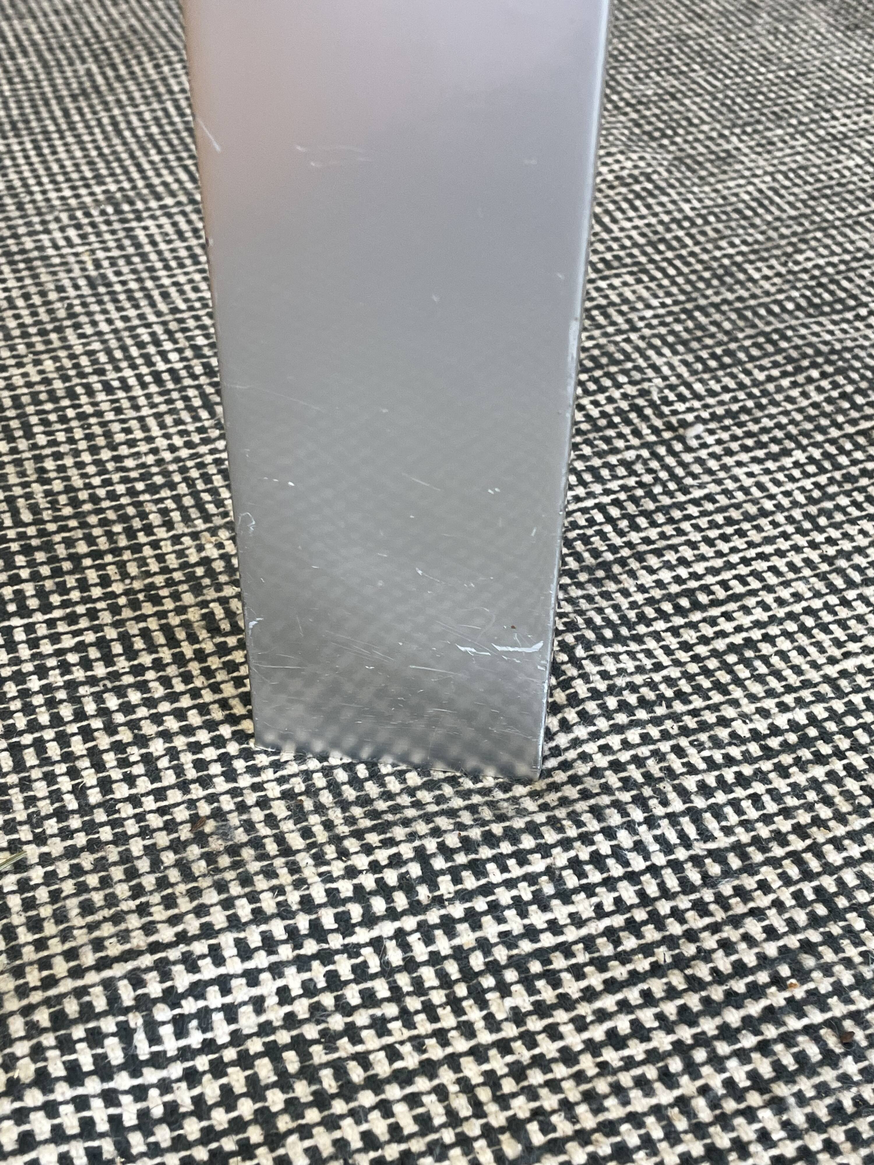 Round dining table with a glass top and brushed metal triangular frame.