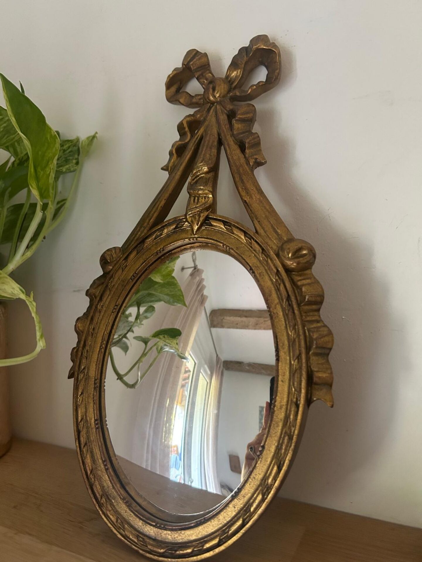 Oval convex witch mirror with golden ribbon mouldings.