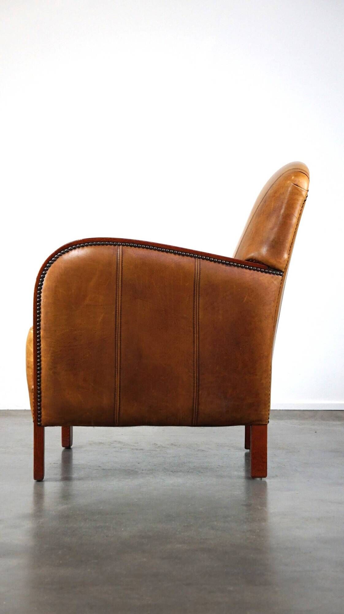 Luxurious cowhide Art Deco design armchair with wooden armrests and cognac-colored leather