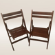 Pair of folding chairs made of dark wood slats.