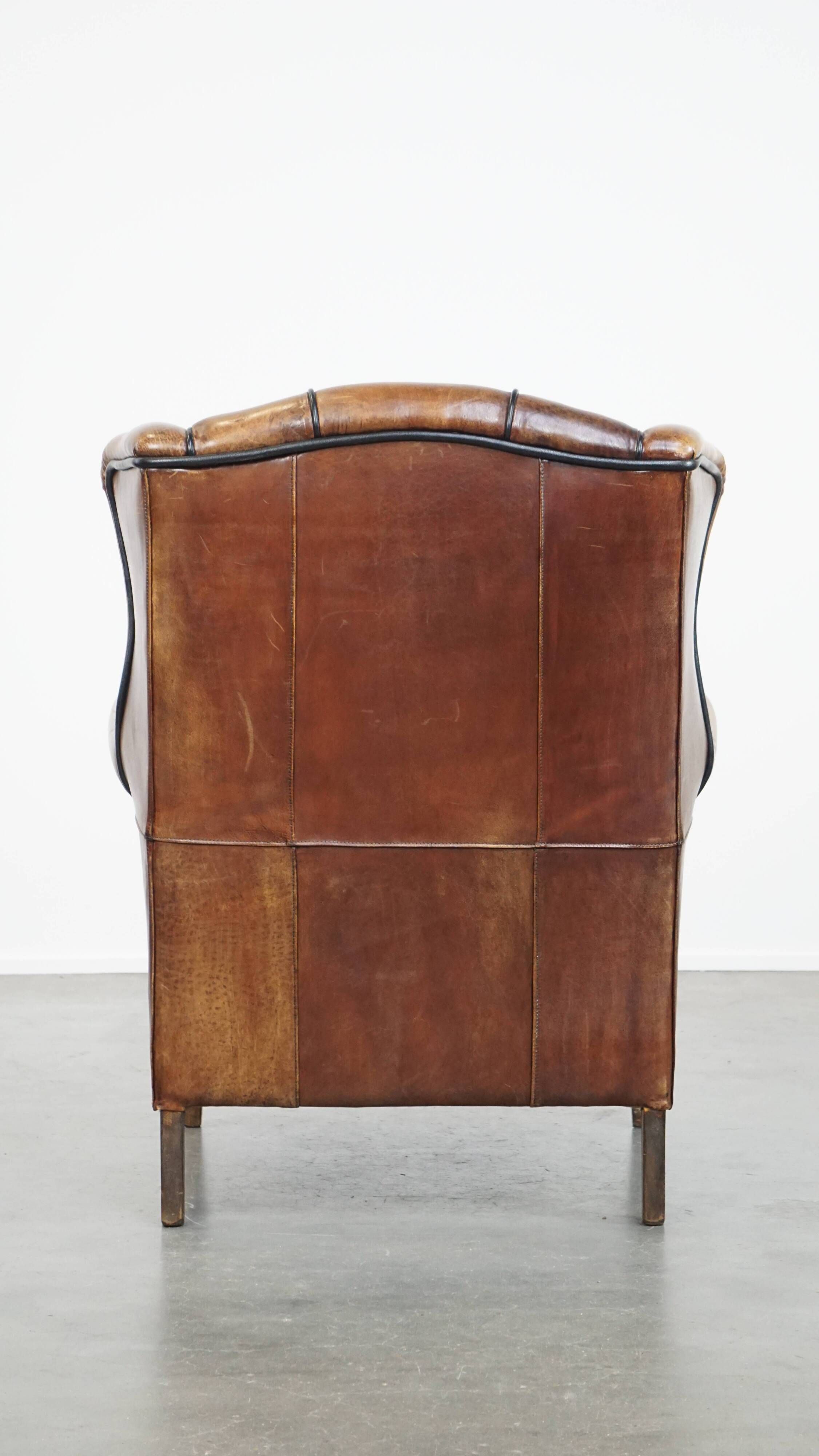 Cognac-colored sheep leather wingback chair finished with black piping