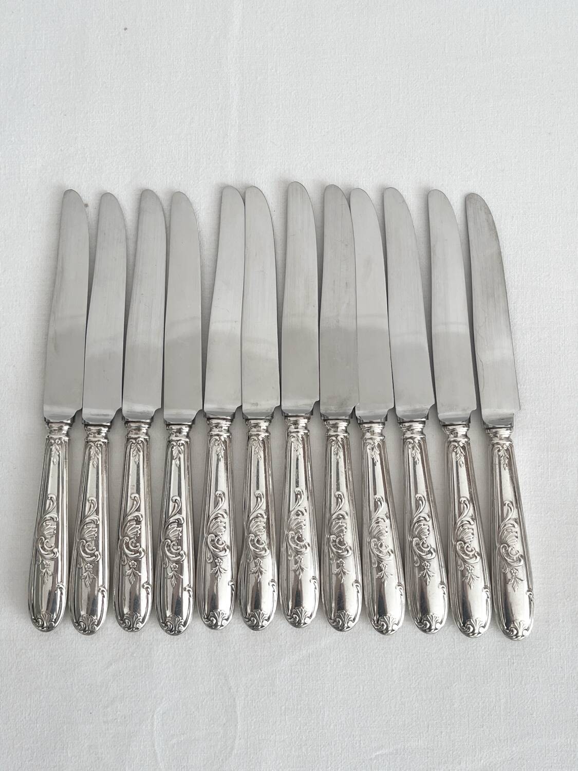 12 antique silver-plated knives with acanthus shell decoration and stainless steel blades.