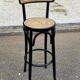 High bistro bar stool in curved black wood with a cane backrest.