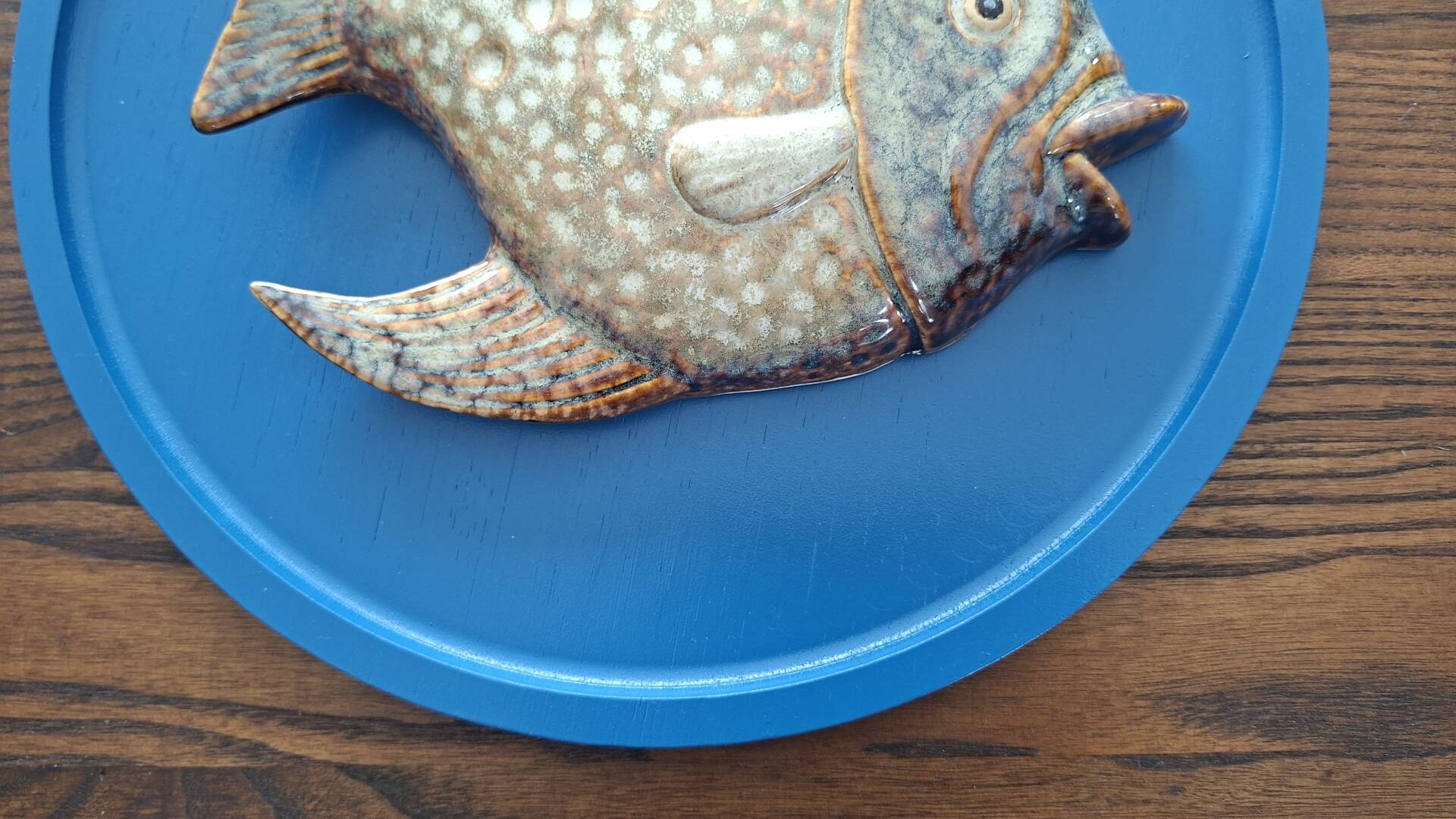 Vallauris ceramic wall sculpture of a relief fish on a blue plaque.