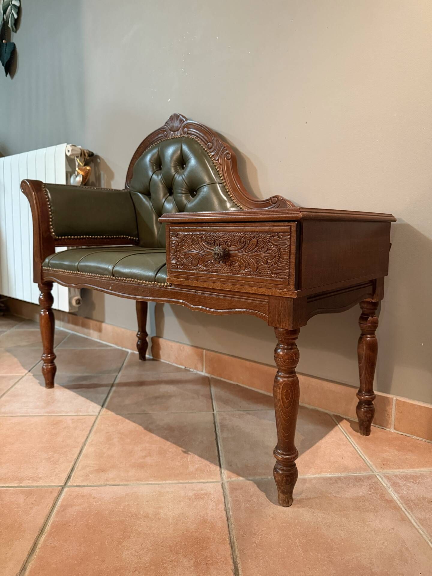Antique carved wooden bench with green upholstered seat and backrest.