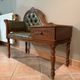 Antique carved wooden bench with green upholstered seat and backrest.