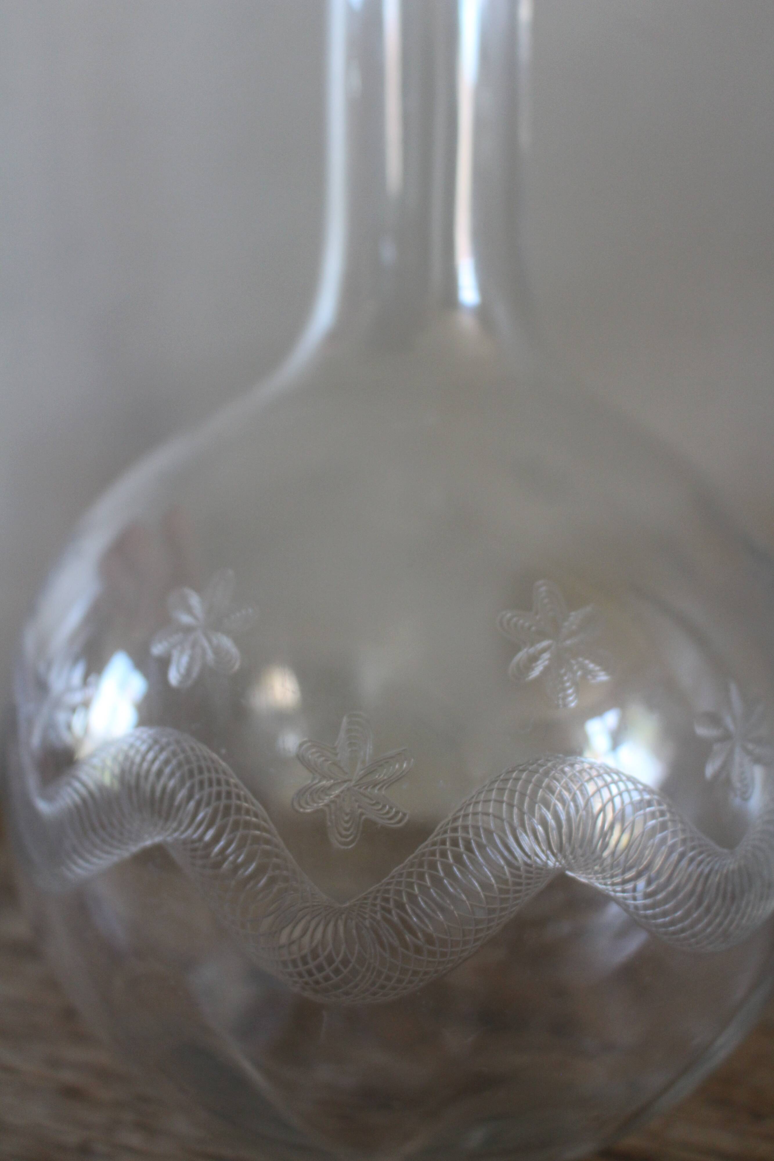 Antique glass carafe with a round belly and floral neck.