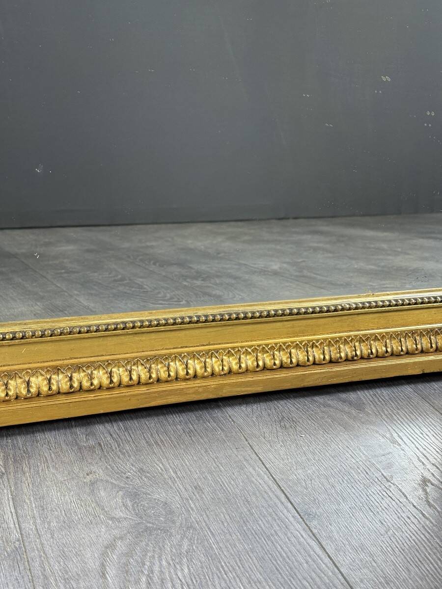 Large antique gilded wooden mirror in Louis XVI style with a sculpted pediment, 19th century.