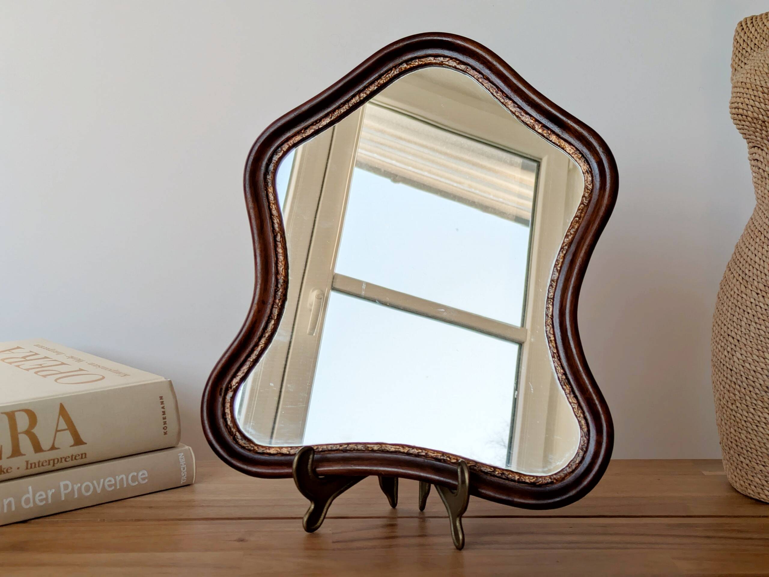 Antique wall mirror in carved wood with a wavy shape and a golden trim.