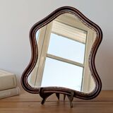 Antique wall mirror in carved wood with a wavy shape and a golden trim.