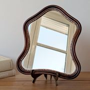 Antique wall mirror in carved wood with a wavy shape and a golden trim.