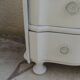 A beautifully crafted crossbow-shaped chest of drawers, finished in pearl grey with a whitewashed top.