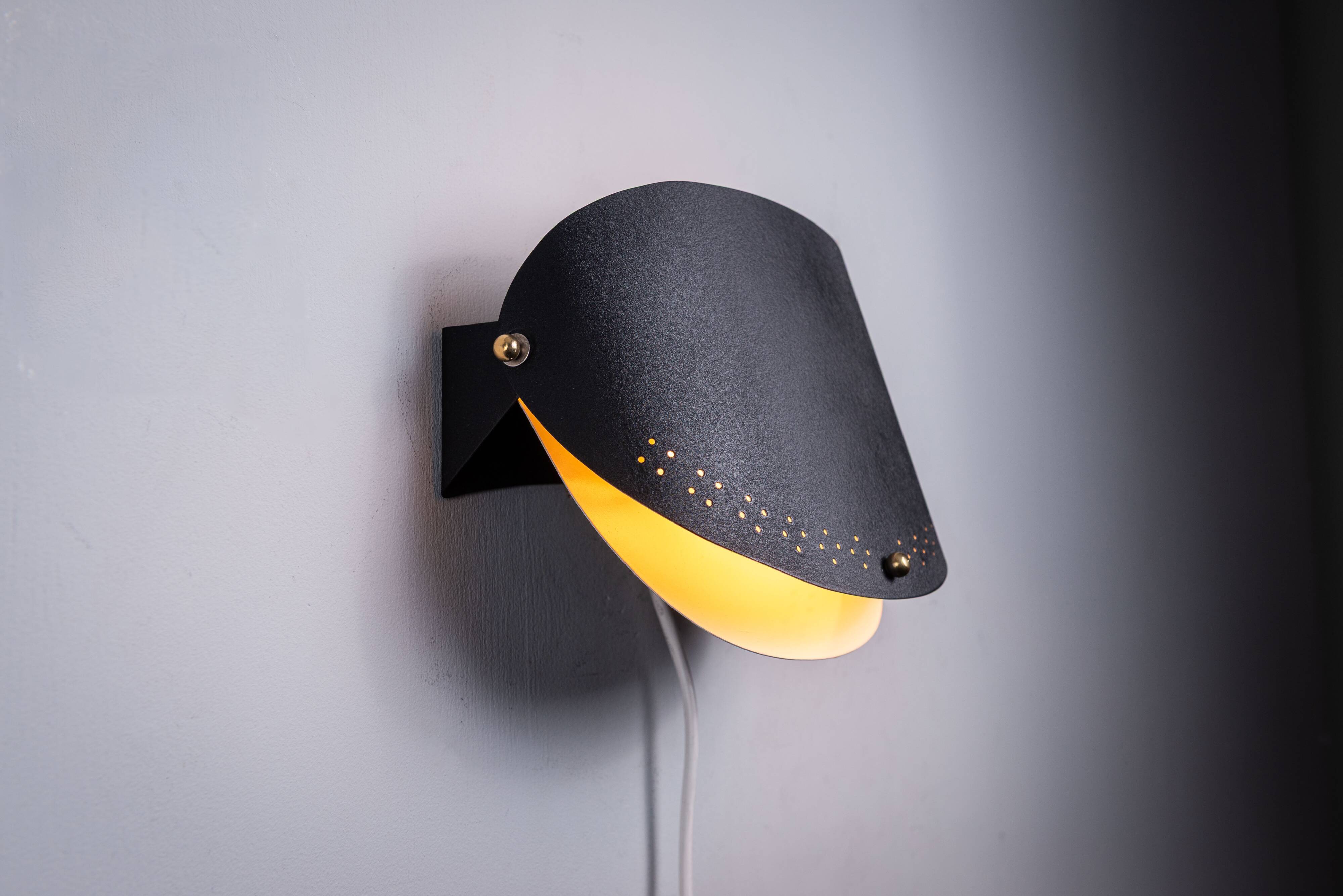 Matte black wall lamps with perforated shades and brass details