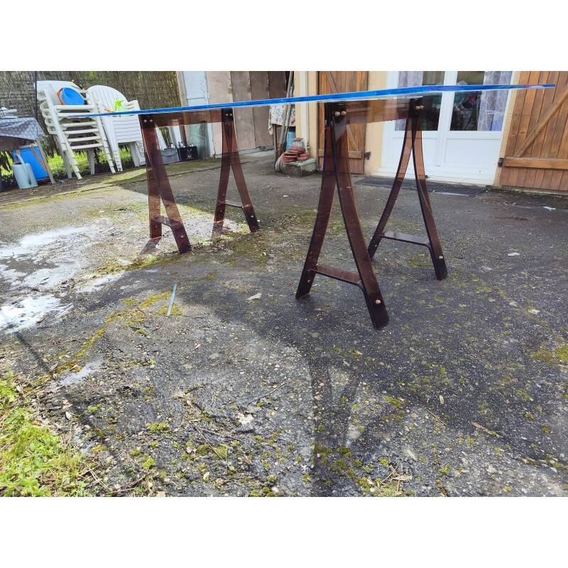 Vintage table with a glass top and smoked plastic trestle legs.