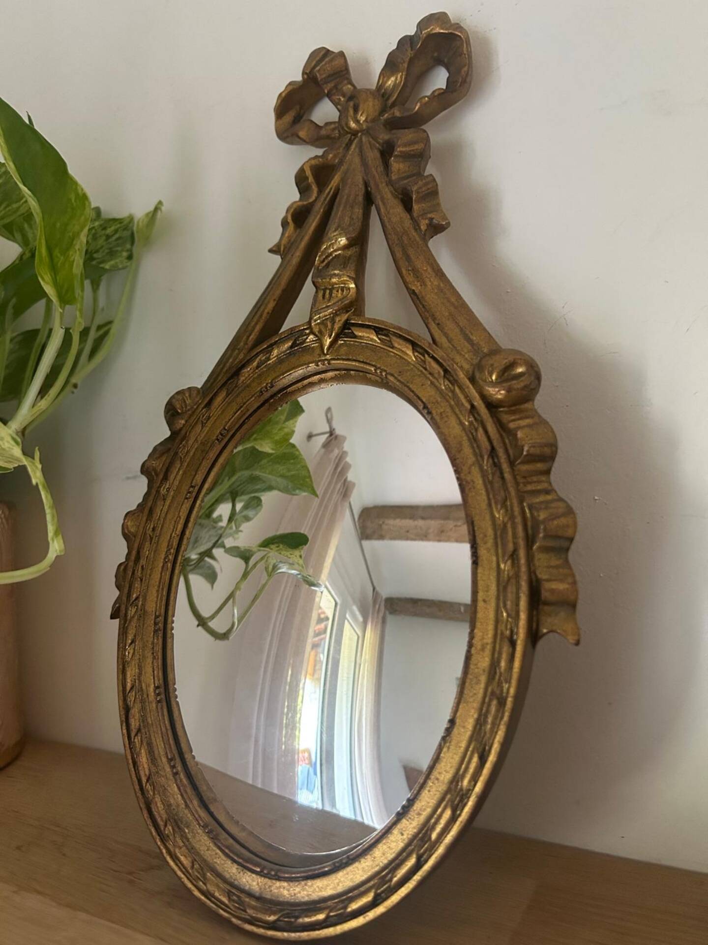 Oval convex witch mirror with golden ribbon mouldings.