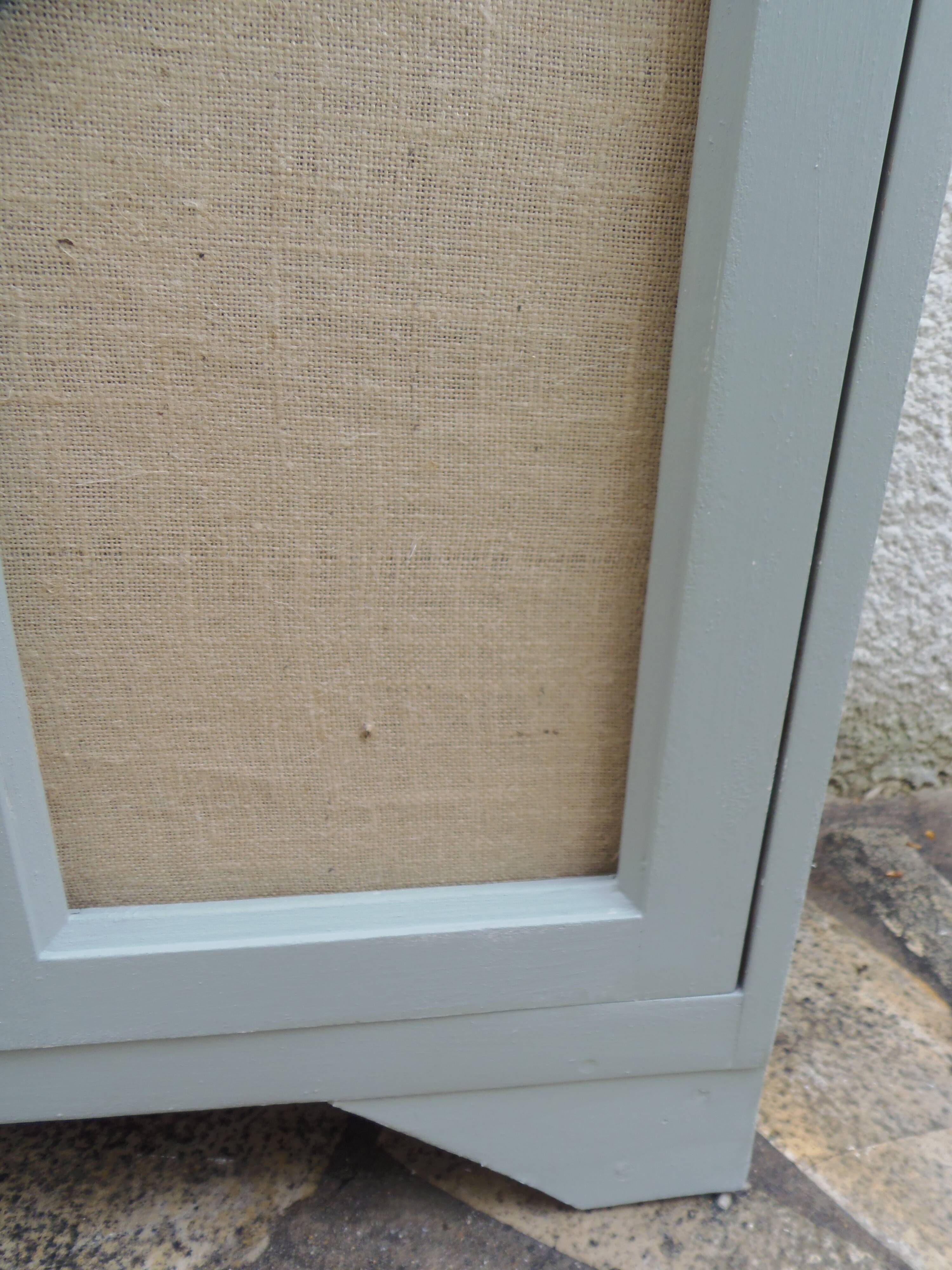 Small vintage green-grey piece of furniture, with 2 doors covered in burlap.
