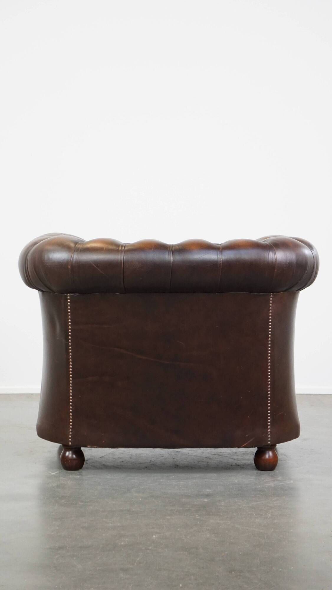 Cowhide English Chesterfield armchair with ball legs and timeless finish