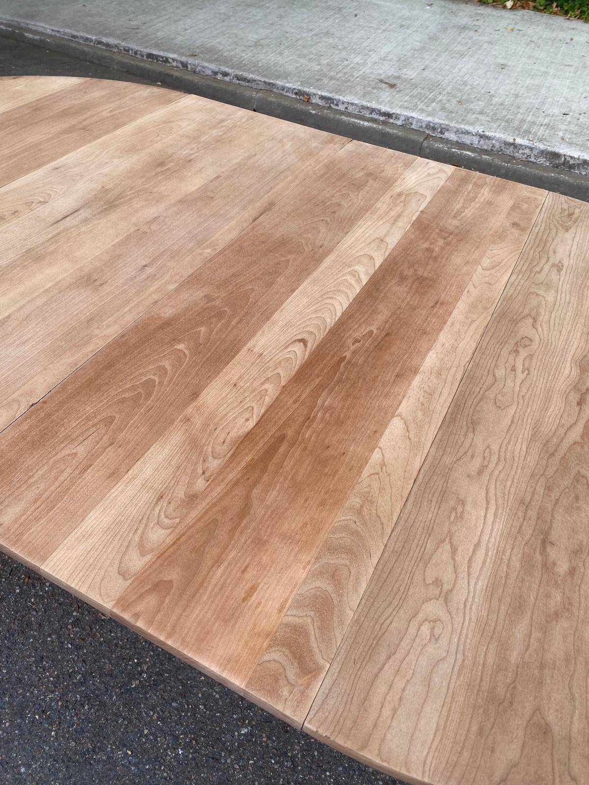 Large extendable round dining table stripped in solid cherry wood with a central leg.