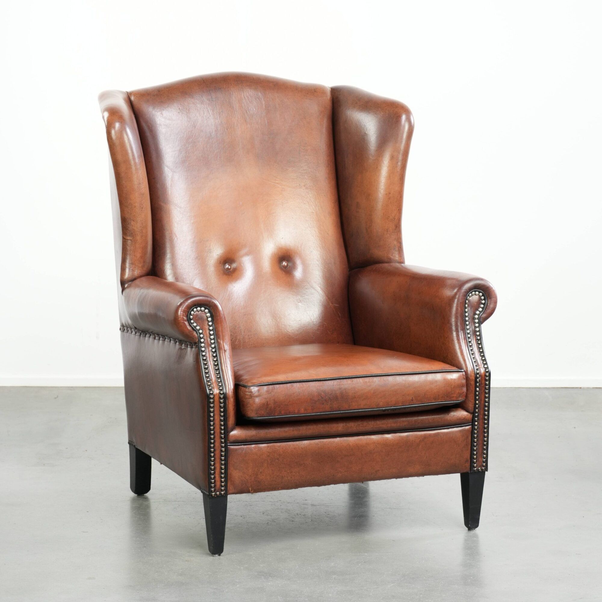 Sheepskin wingback armchair in a warm cognac colour with refined nailhead trim