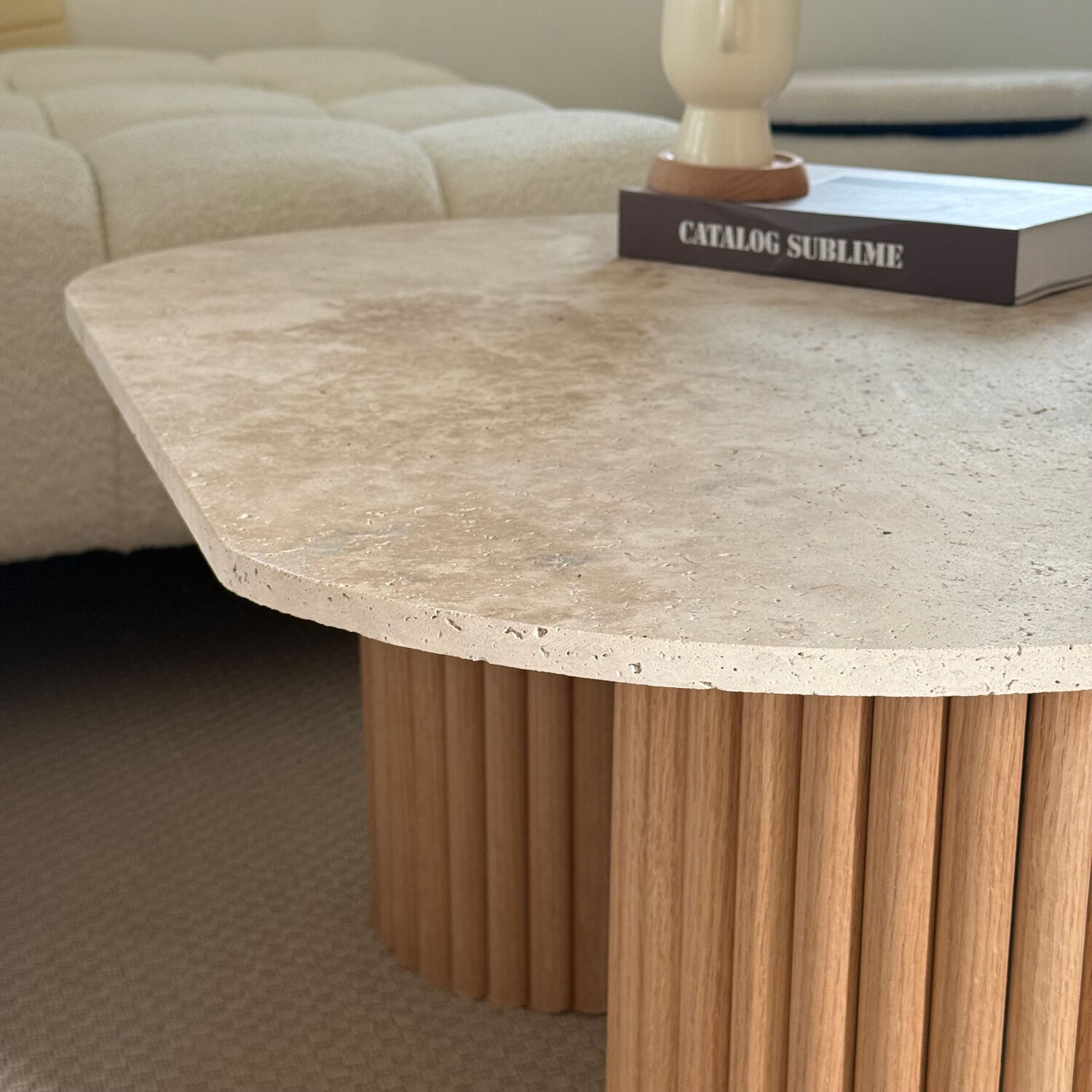 Oval coffee table in travertine and raw fluted wood.