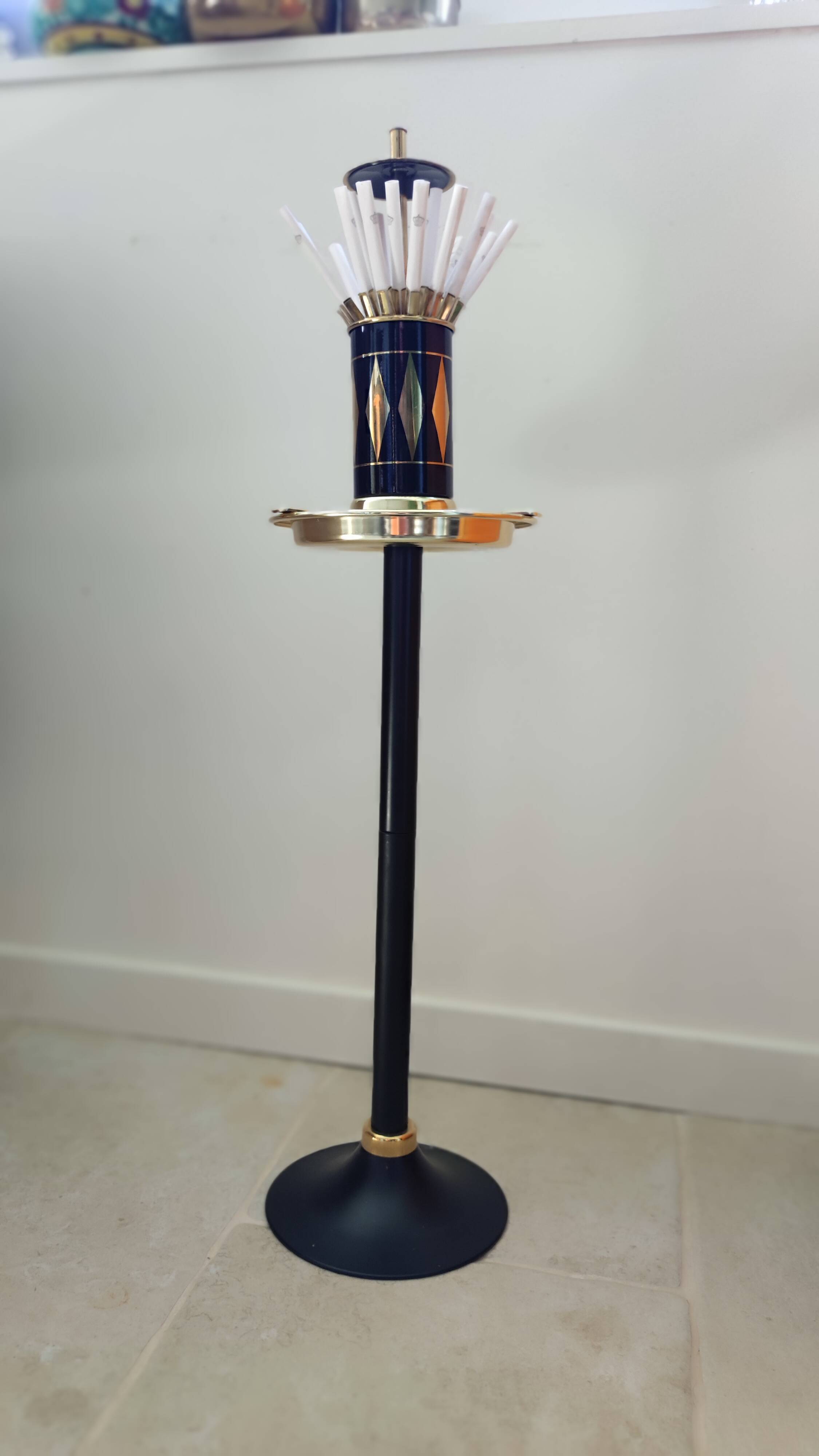 Vintage floor ashtray with a gold and black metal cigarette dispenser.