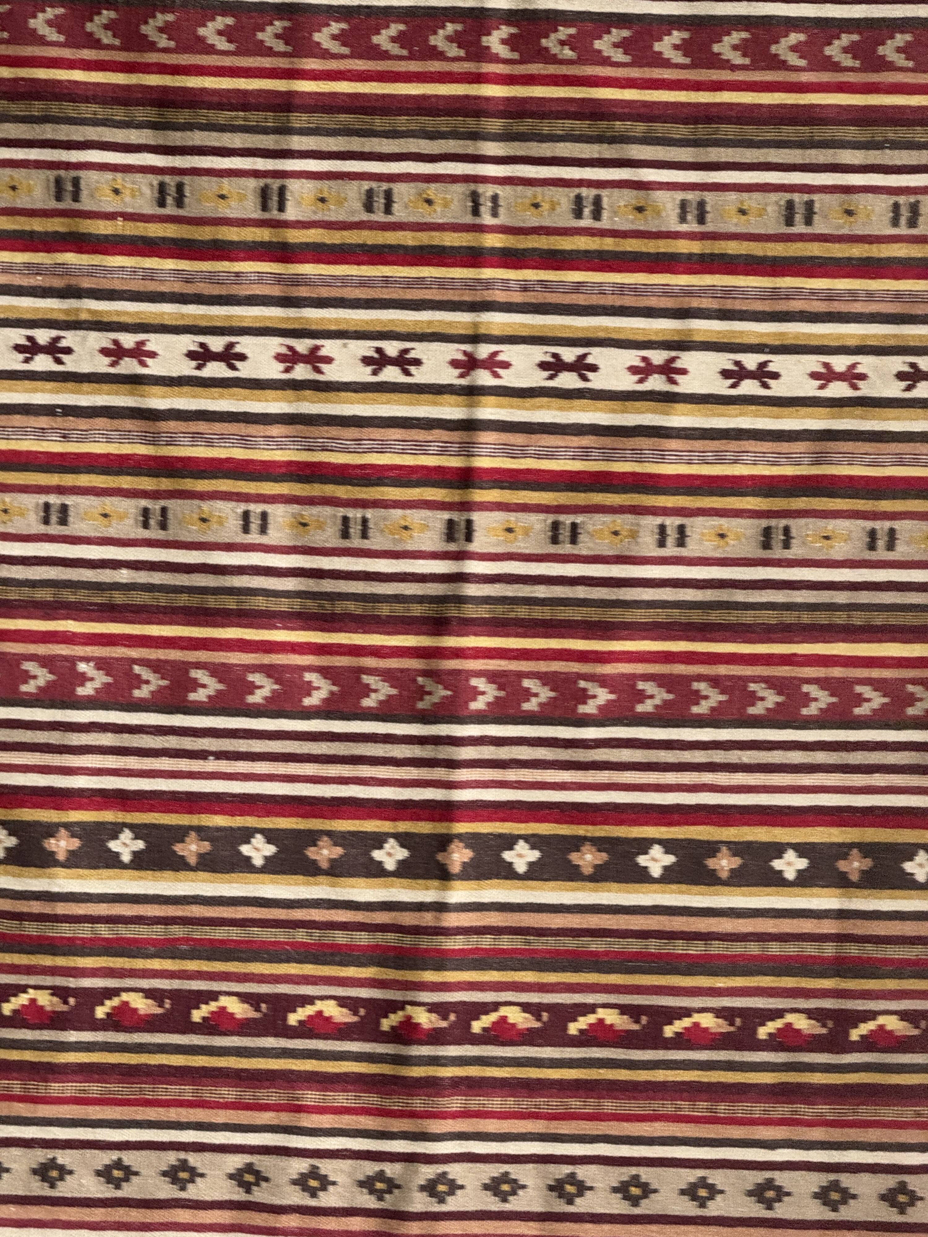 Large Indian rug with red, yellow, and white stripes and geometric fringes.