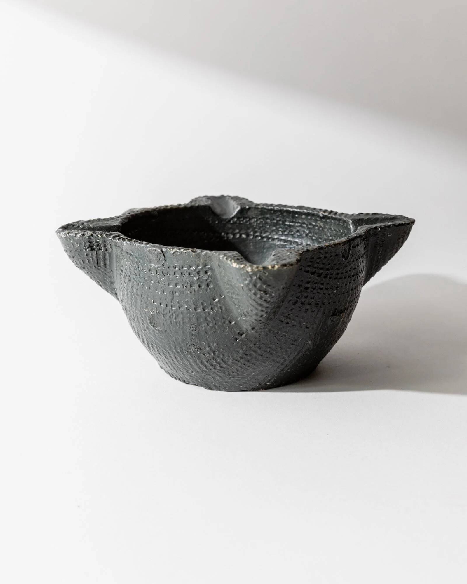 Vintage ceramic ashtray from the 1960s, black, hand-sculpted texture, organic shape.