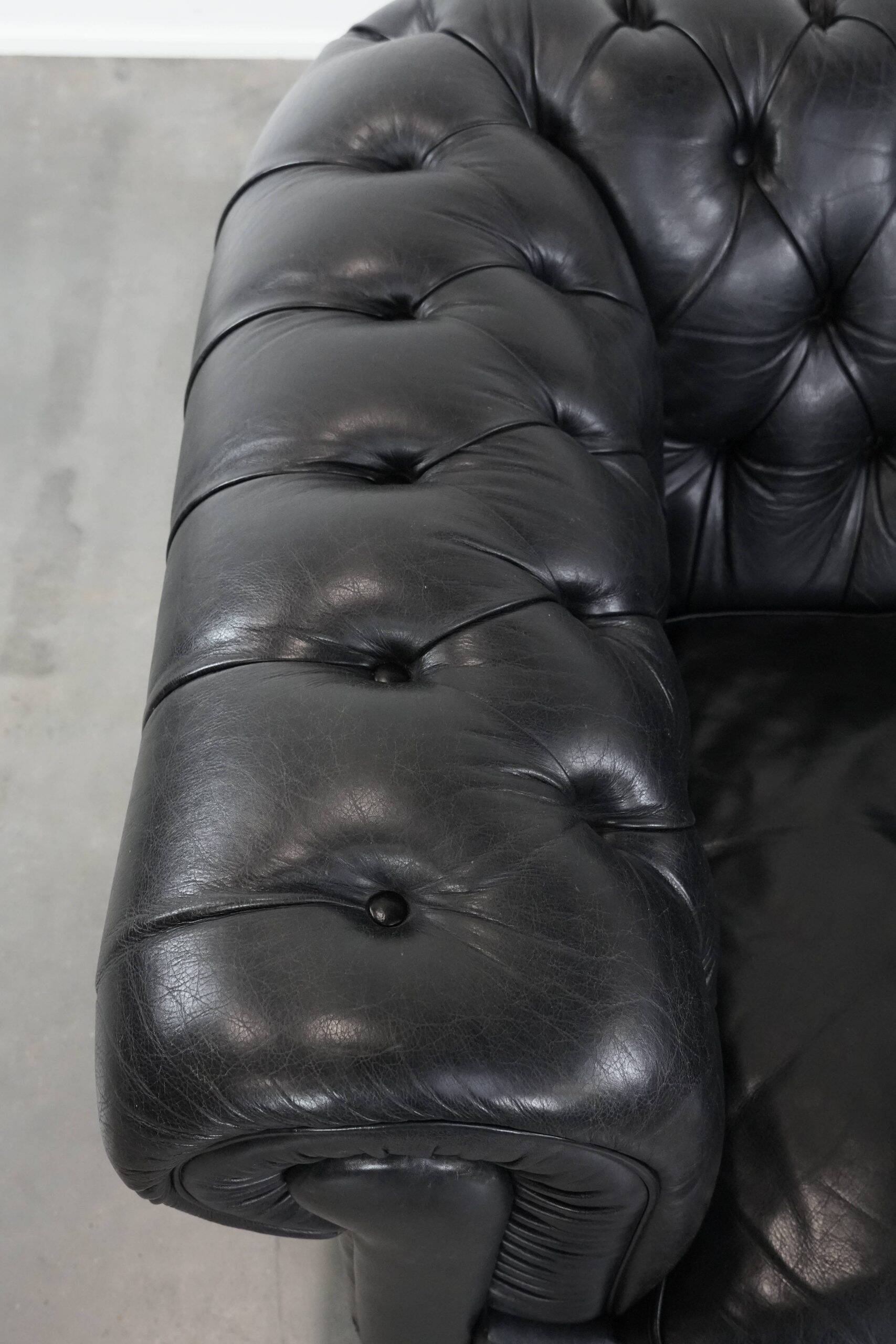 Ensemble composé d'un canapé chesterfield noir, d'un fauteuil et d'un pouf.