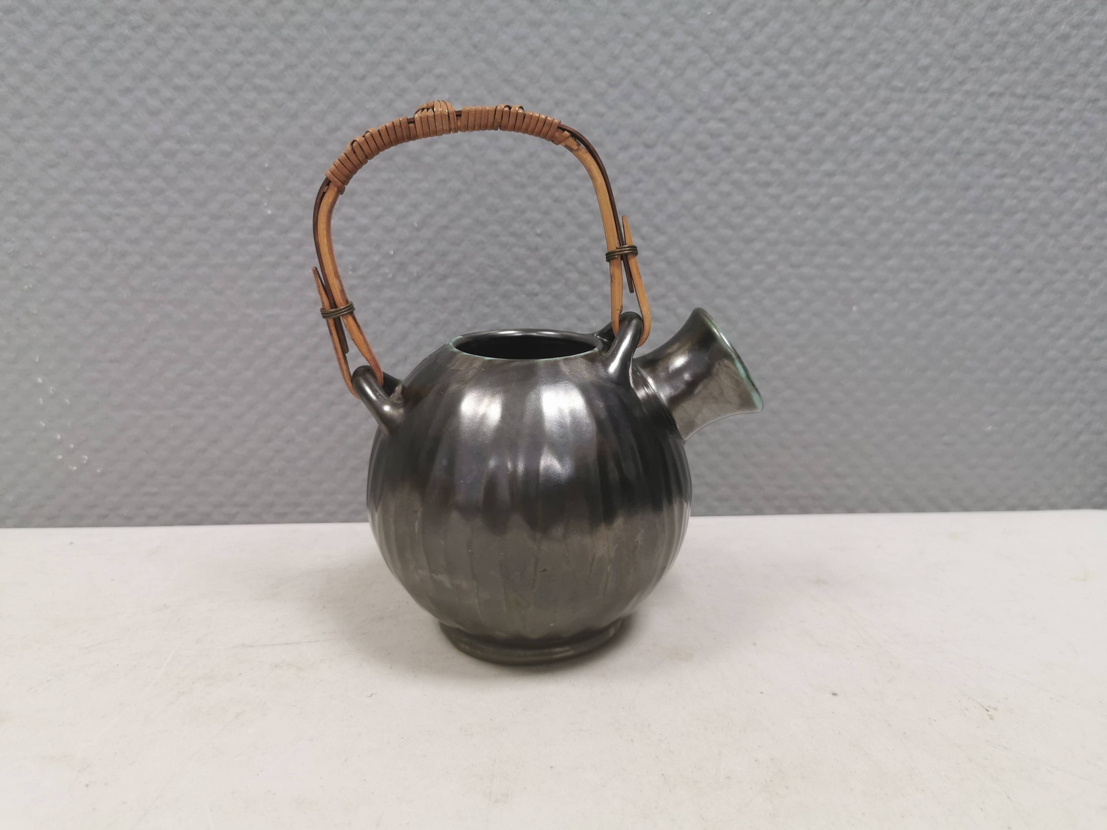 A ceramic jug with a metallic glaze and a handle made of woven raffia.