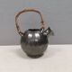 A ceramic jug with a metallic glaze and a handle made of woven raffia.