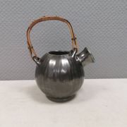A ceramic jug with a metallic glaze and a handle made of woven raffia.