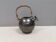 A ceramic jug with a metallic glaze and a handle made of woven raffia.