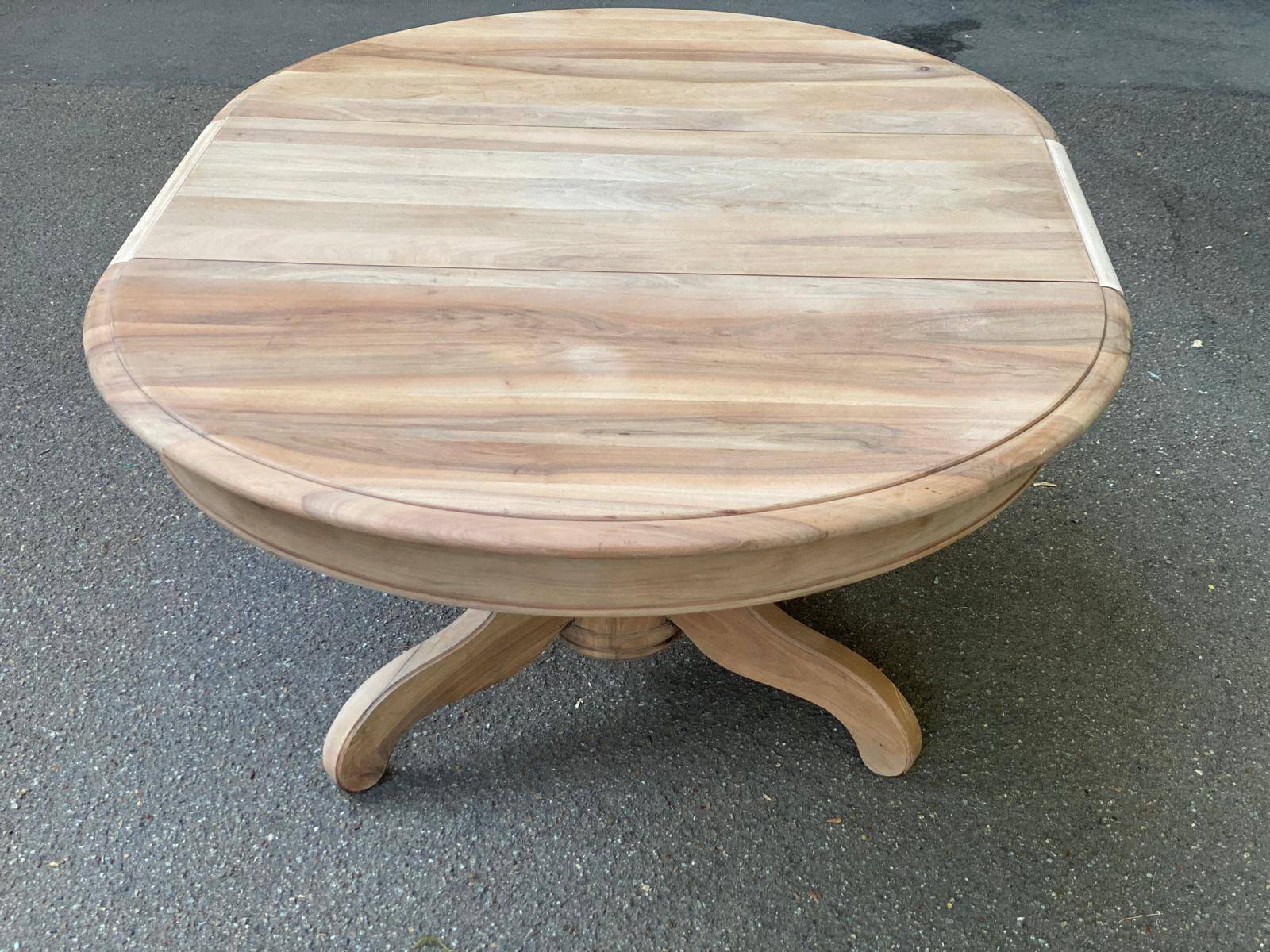 Round extendable dining table stripped in solid raw walnut with a central leg.