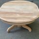 Round extendable dining table stripped in solid raw walnut with a central leg.