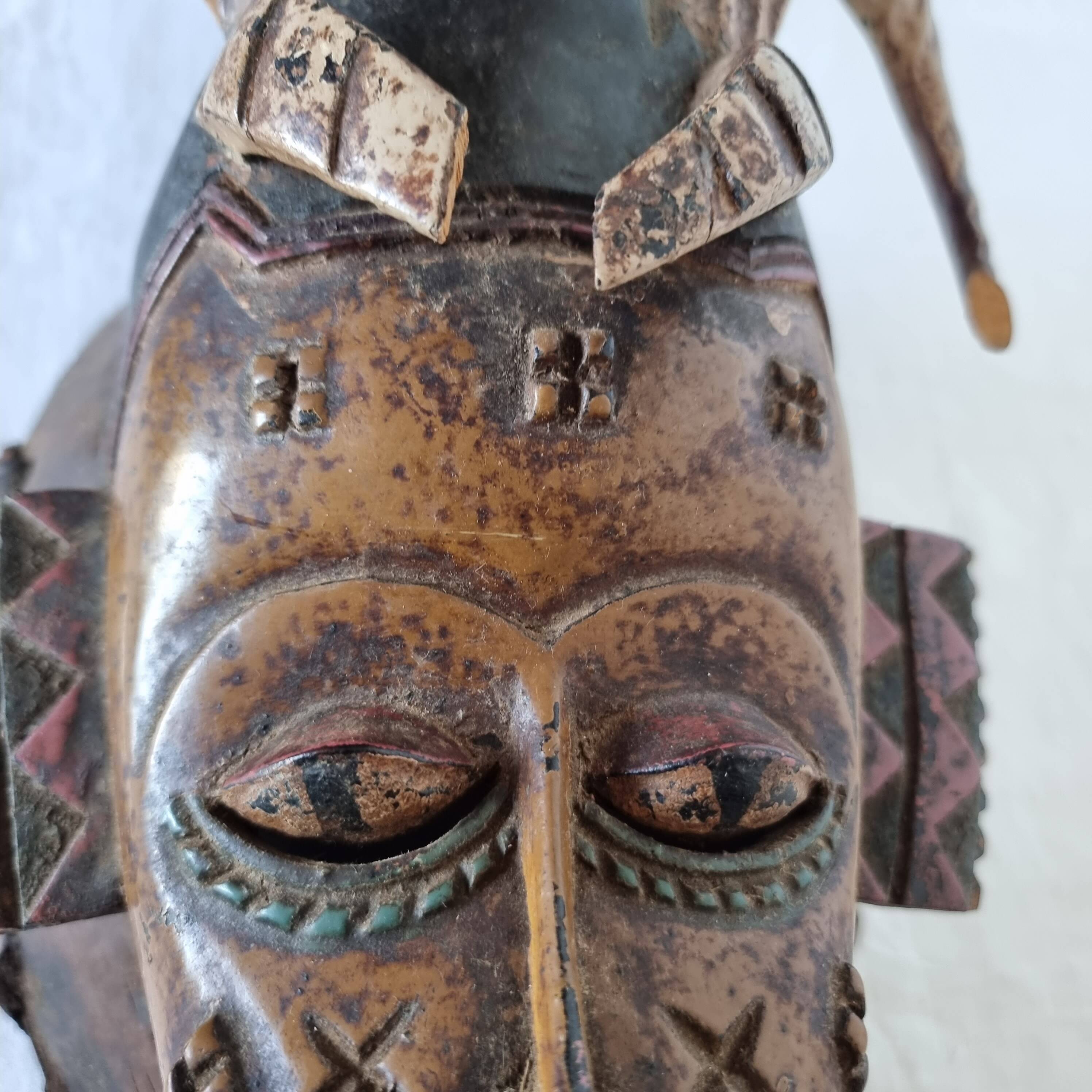 A large Senufo mask made of colored wood, decorated with an anthropomorphic figure