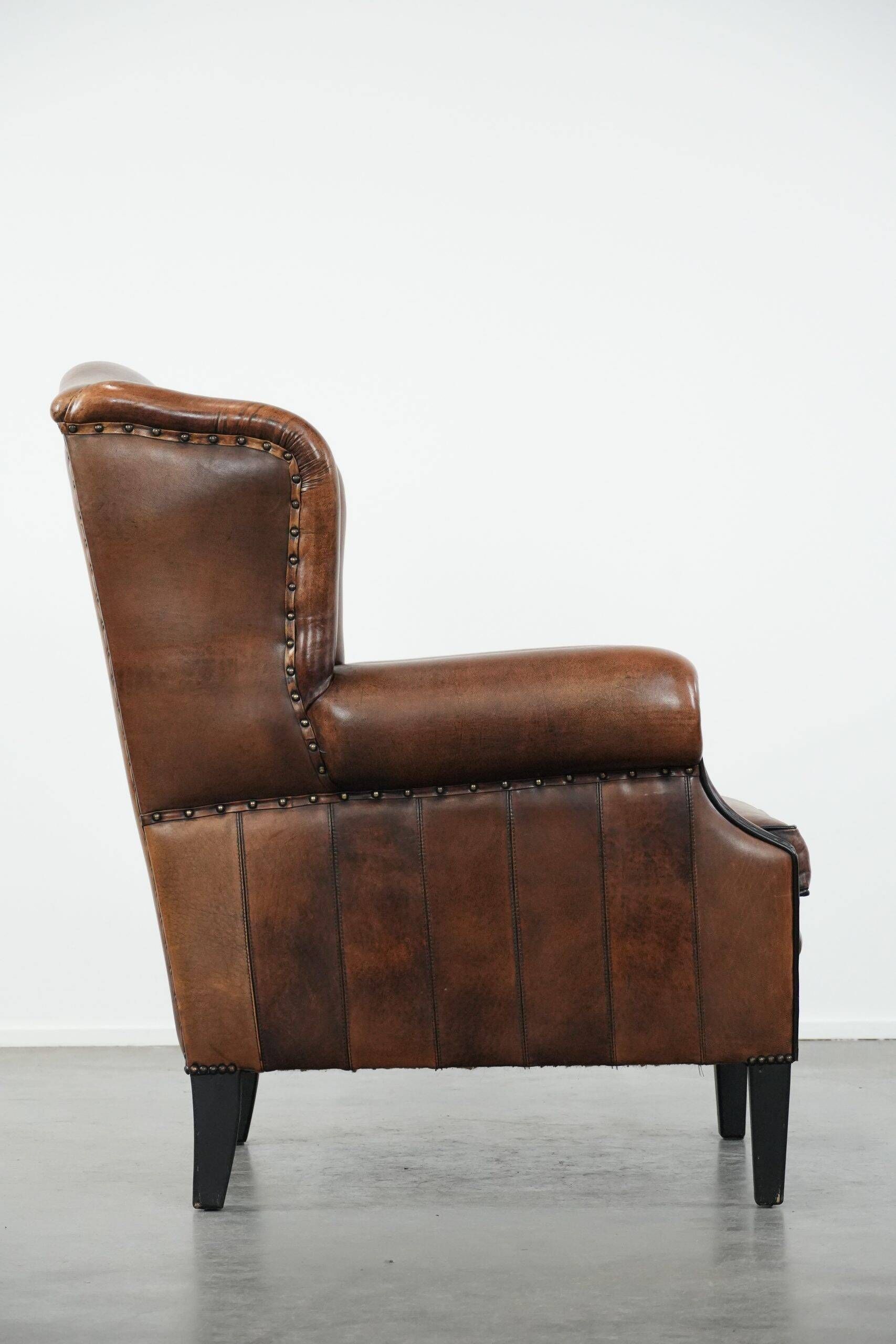 Sheepskin wingback armchair with decorative nails and black piping