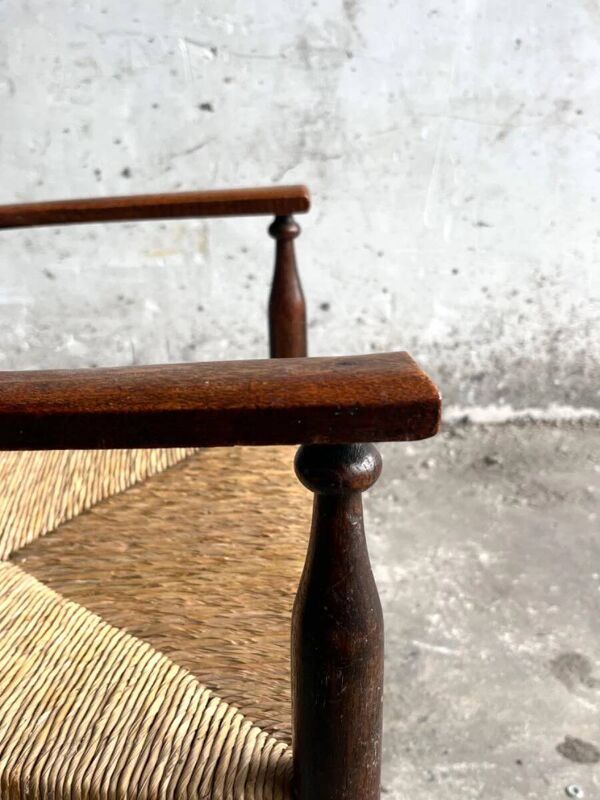 Fauteuil Arts & Crafts en bois massif brun foncé, avec assise en jonc naturel et dossier haut.