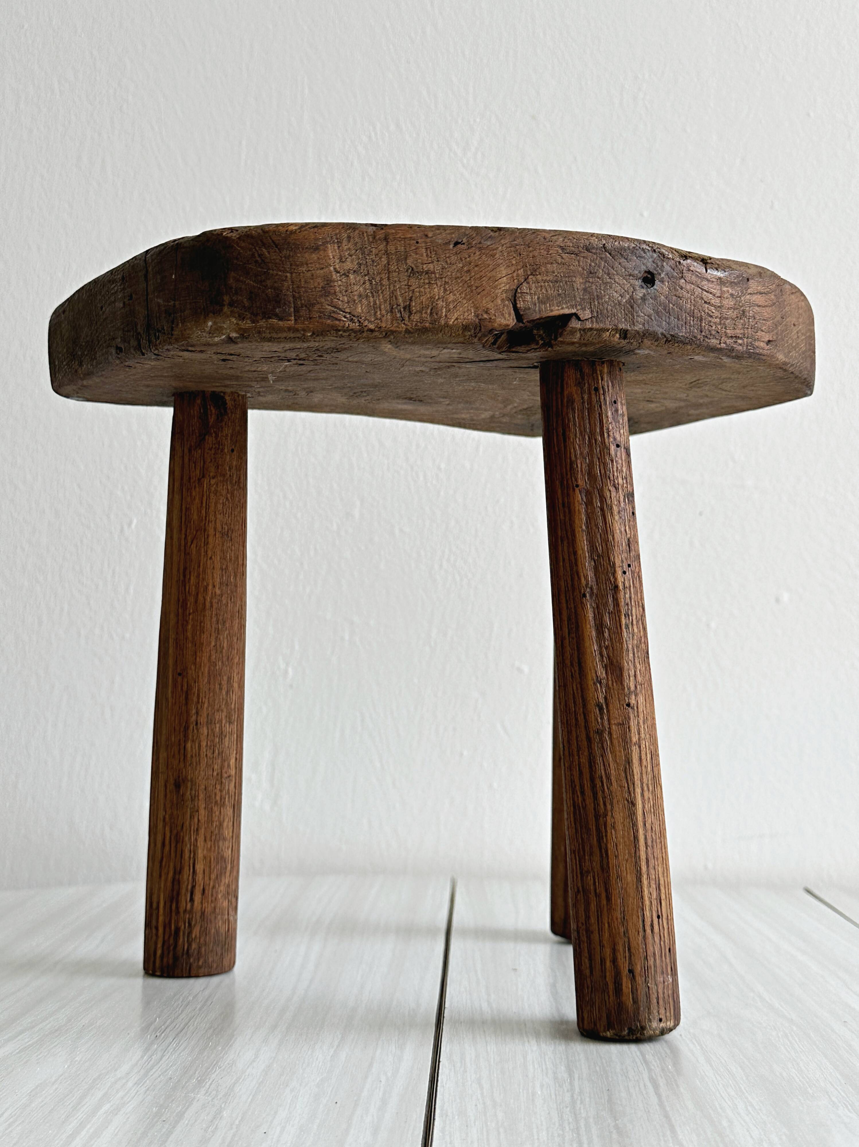 Antique three-legged stool made of raw solid wood.