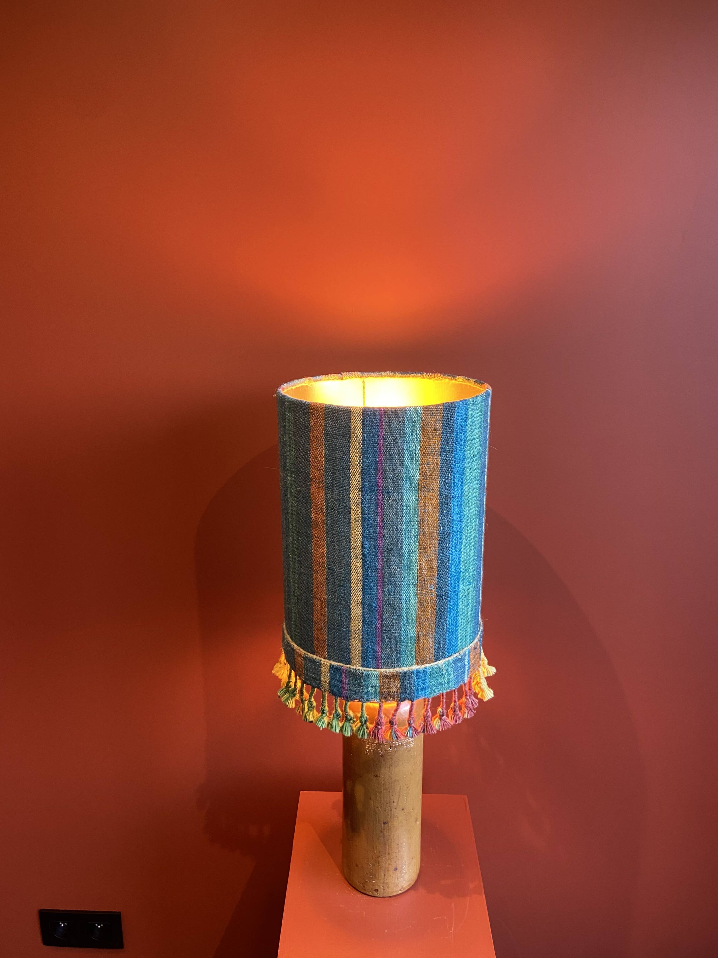 "Stoneware Bottle Lamp" with a multicoloured blue lampshade handwoven in India.