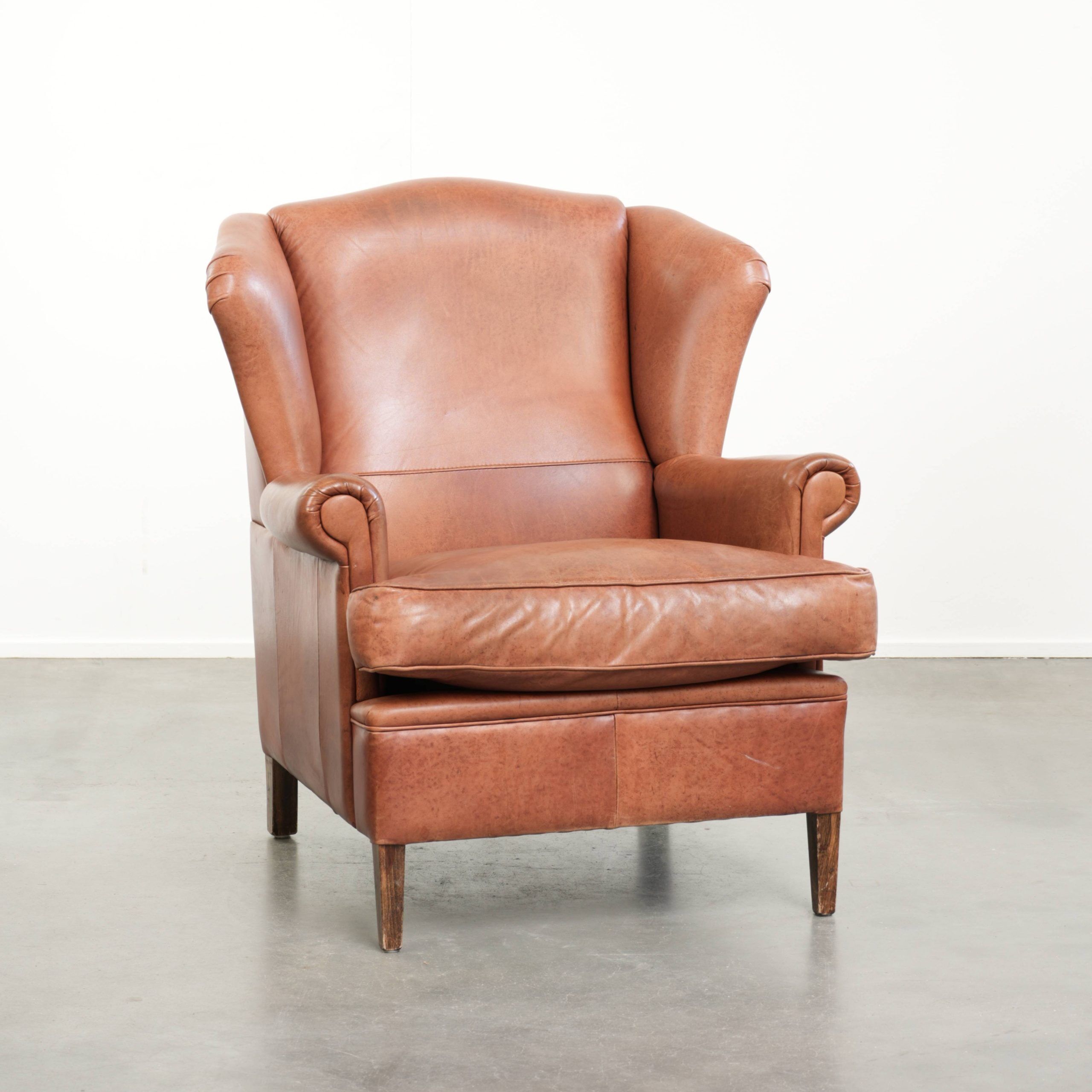Light cognac-coloured cow leather wingback armchair with matching piping