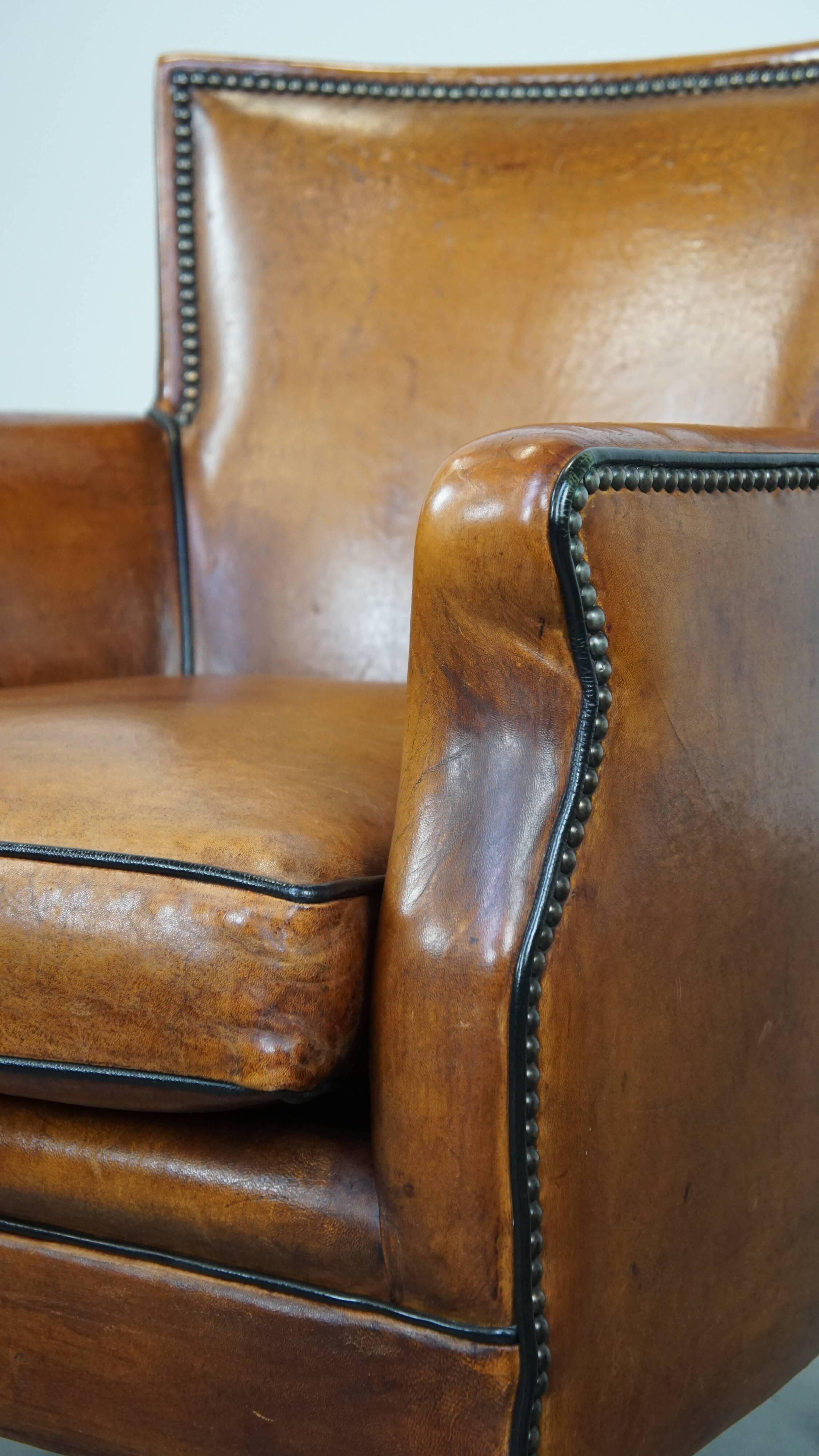 Cognac-colored sheepskin armchair with black piping and decorative nails