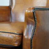 Cognac-colored sheepskin armchair with black piping and decorative nails