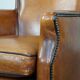 Cognac-colored sheepskin armchair with black piping and decorative nails