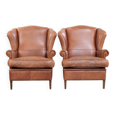 Fauteuils à oreilles en cuir de vache de style anglais avec passepoil assorti.