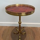 A round, neoclassical-style brass side table with a base decorated with dolphins and a red celluloid top encircled by an openwork gallery, attributed to the House of Jansen.