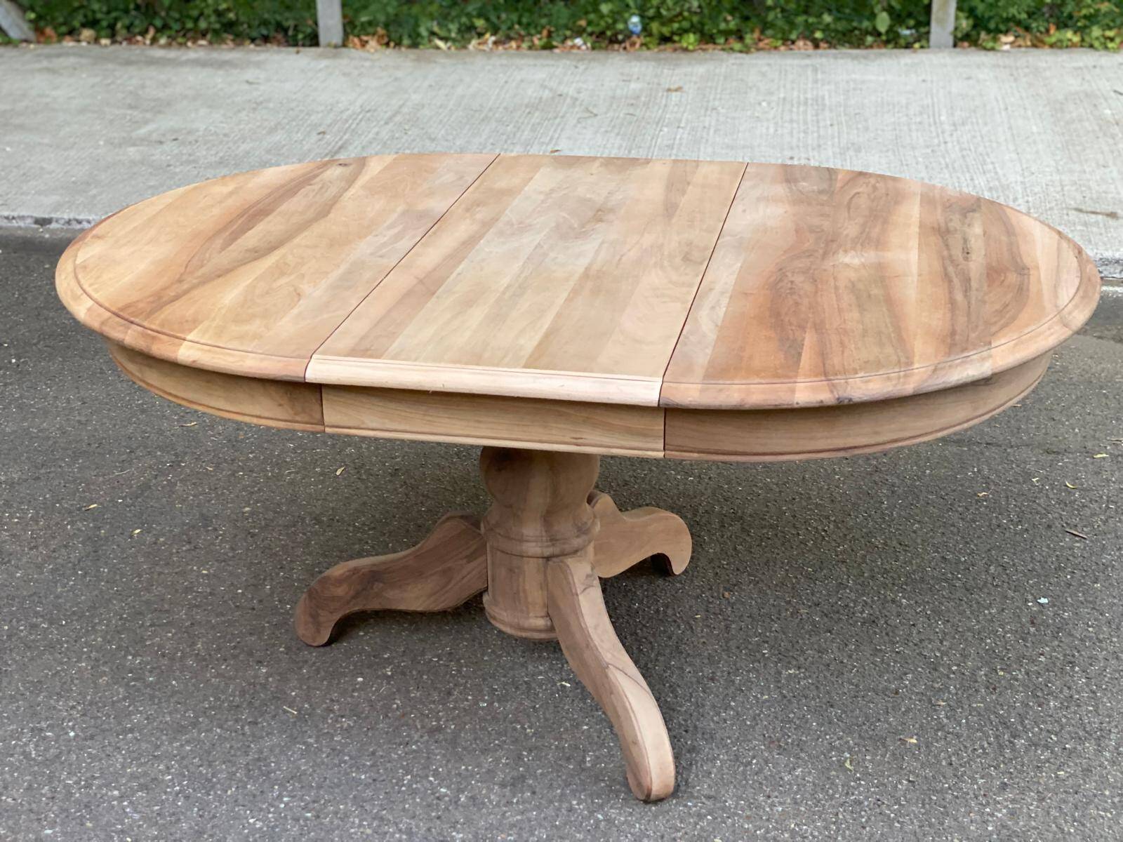 Round extendable dining table stripped in solid raw walnut with a central leg.