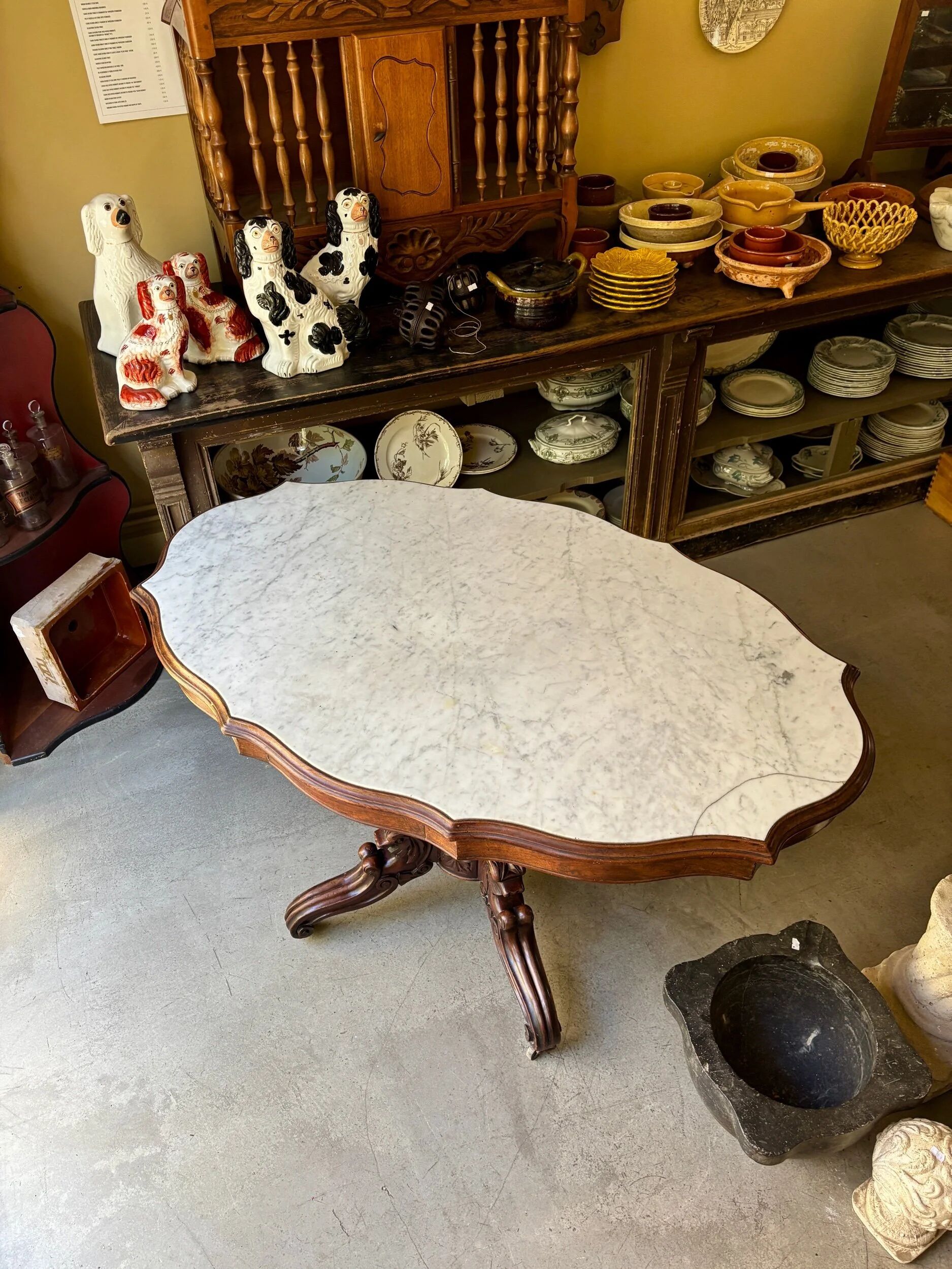 Table with a carved wooden frame and grey marble top on wheels, measuring 130 x 82 cm.