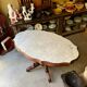 Table with a carved wooden frame and grey marble top on wheels, measuring 130 x 82 cm.