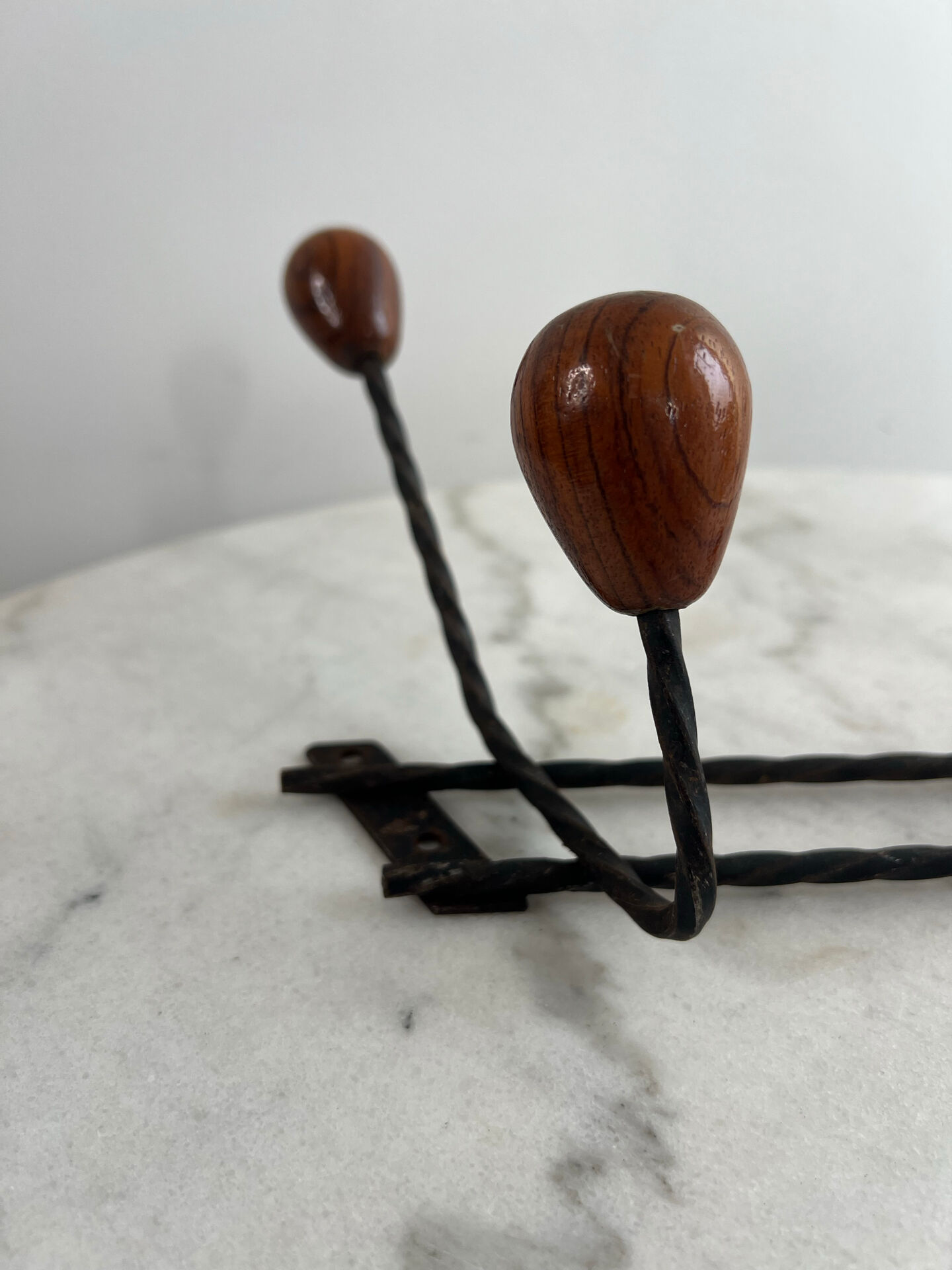 Wall-mounted coat rack in wrought iron with turned wooden knobs.