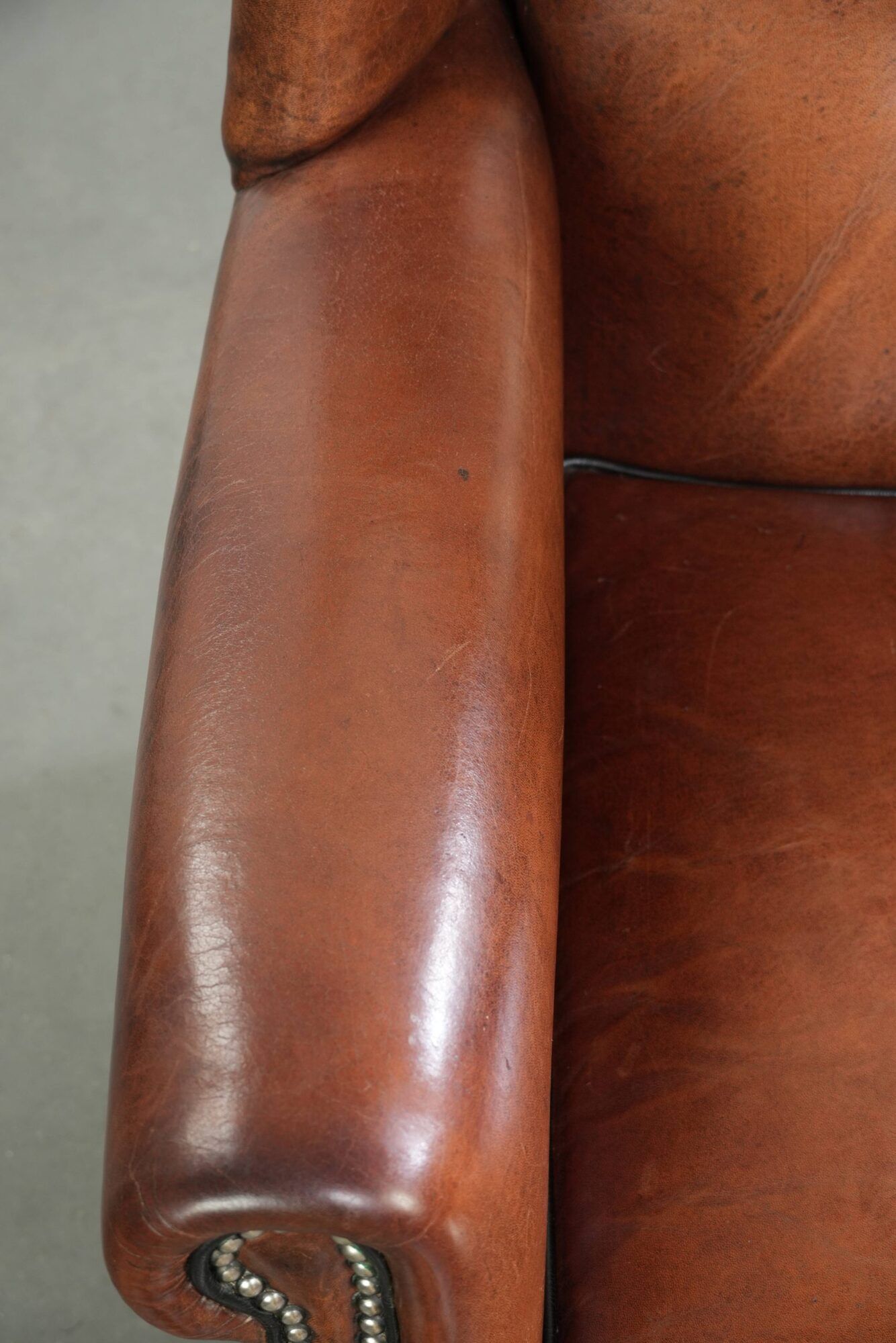 Sheepskin wingback armchair in a warm cognac colour with refined nailhead trim
